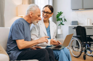 A hospice caregiver and a senior man looking at a laptop together during a home care consultation.